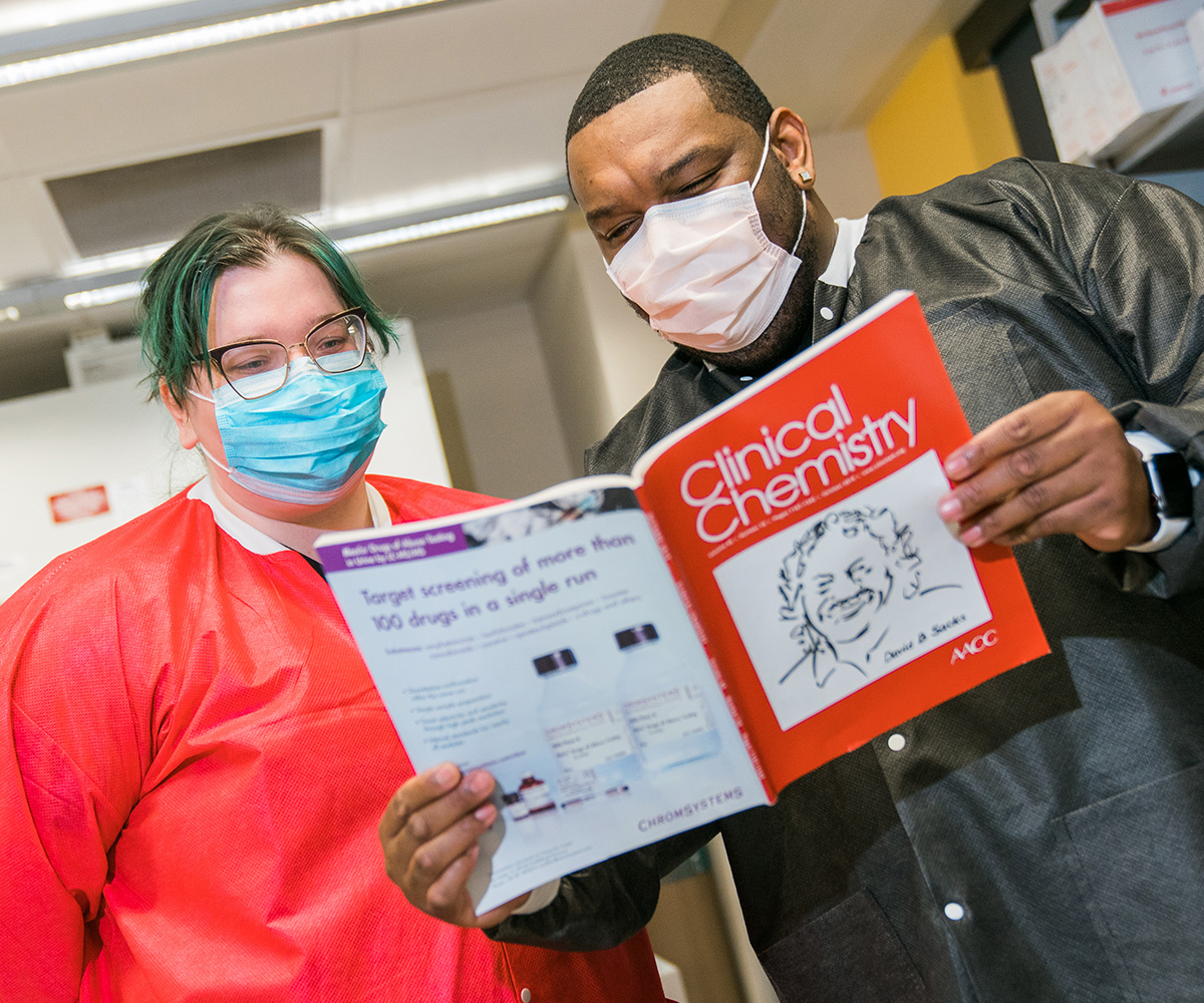 Two masked lab techinicians reading a Clinical Chemistry journal