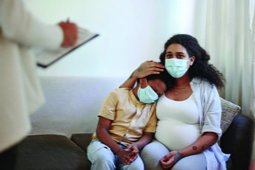 A woman in a mask sitting on a couch holding her son.