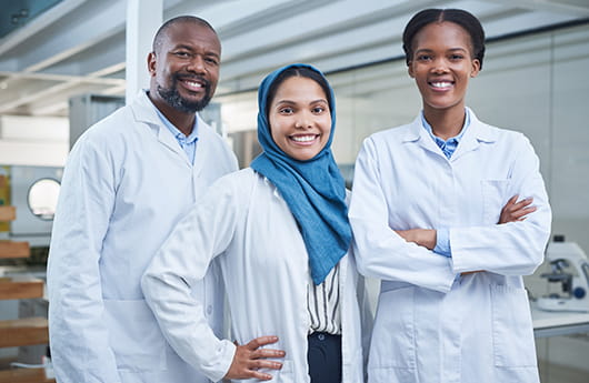 A diverse trio of laboratory medicine professionals standing and smiling together.
