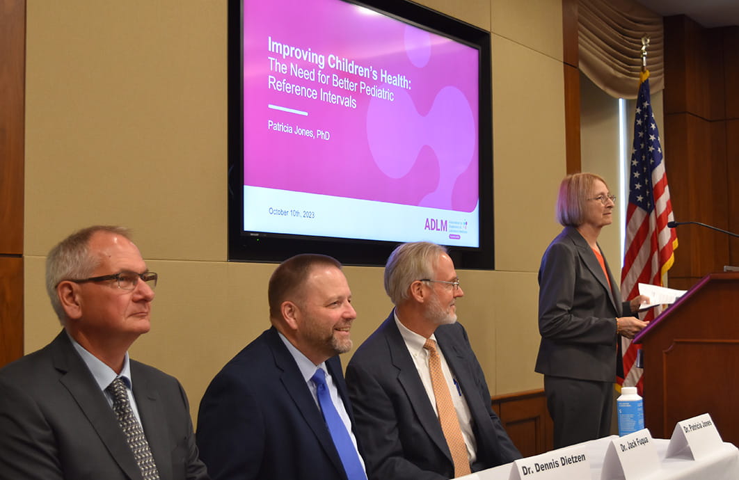 Row of speakers at a conference with a large TV screen mounted behind them. 