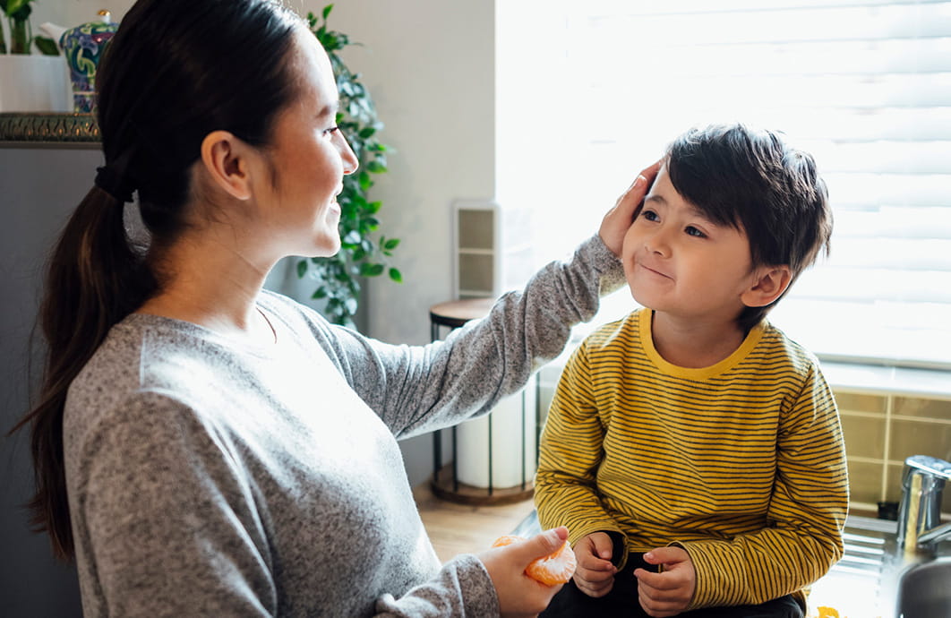 Woman stroking the hair of smiling male toddler sitting on desk