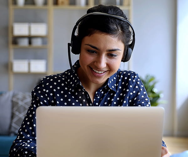 A smiling woman wearing headphones looks at a laptop.