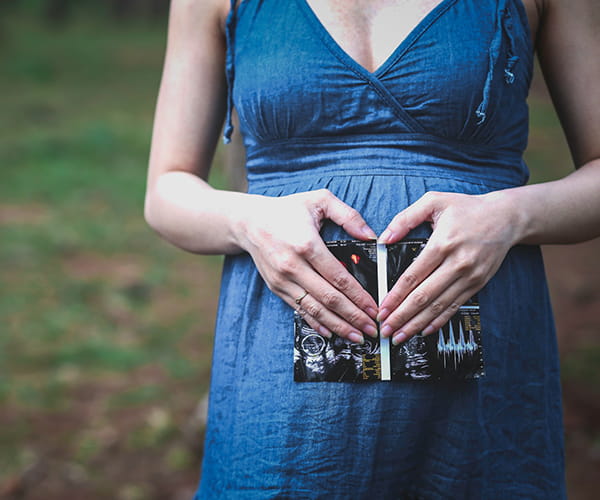 A woman in early pregnancy holds an ultrasound image against her stomach.
