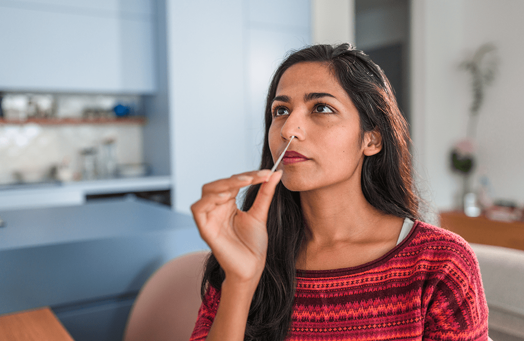 A woman inserts a testing swab in one of her nostrils.