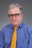 An older man wearing glasses, with blue shirt and yellow tie