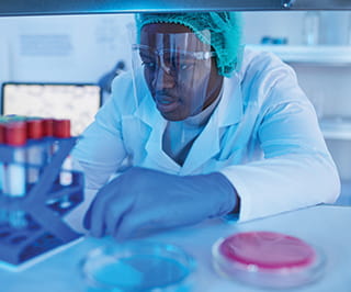 laboratorian in protective gear looks at sample test tubes