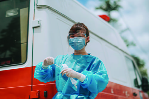 A masked female in a surgical gown holding a COVID-19 sample kit