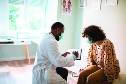 A male doctor pointing at a piece of paper for a female patient sitting on a doctor bed 