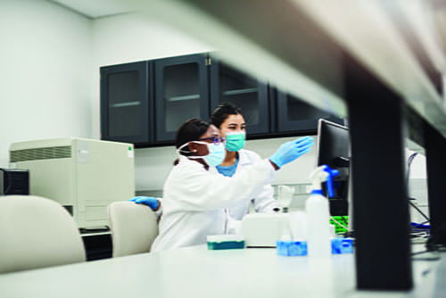 Two masked, female laboratorians looking at a computer screen 