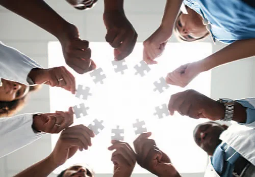 Laboratorian hands in a circle each holding puzzle pieces.