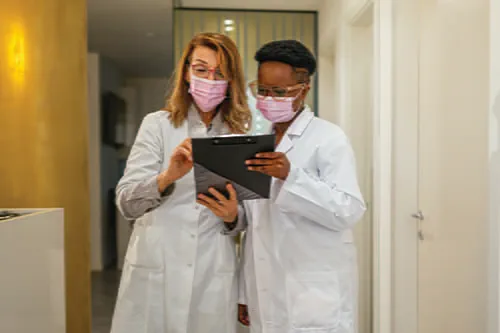 Two female laboratorians in masks holding and looking at a clipboard.