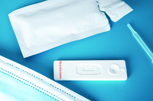 A SARS-CoV-2-Ag antigen test placed in between a blue mask and the test packaging.
