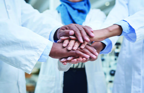 Laboratorians in lab coats putting their hands in the center