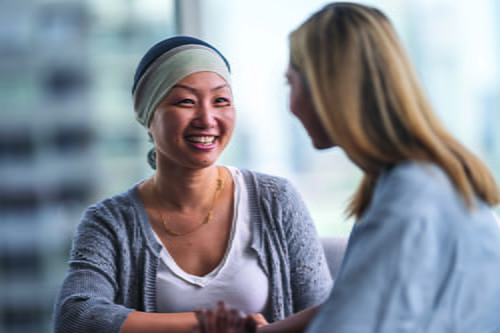 An Asian woman sitting at a table and smiling at a woman healthcare professional sitting next to her