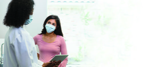 A woman laboratorian holding a clipboard and speaking to a woman patient.