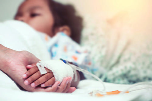 A child in a hopstial bed holding an adults hand.
