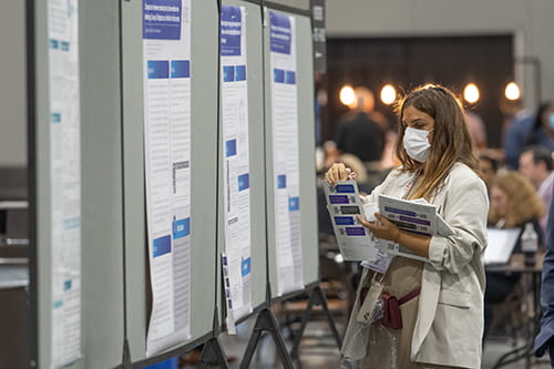 A masked female holding booklets in front of multiple posters