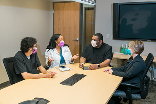Lab professionals in masks sitting around a table talking