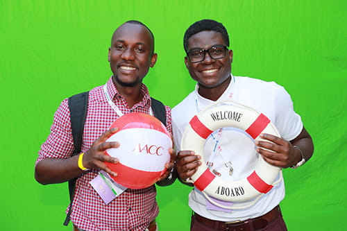 Two men posing and smiling at the camera while one holds an AACC beach ball and the other holds a buoy that reads "Welcome Aboard"