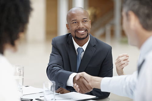 An African American man smiling and shaking the hand of a white man.