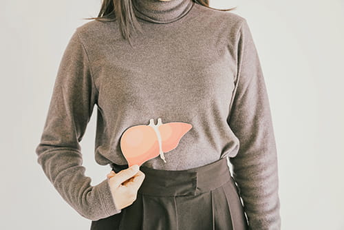 An image of a woman standing and holding an image of a liver against her stomach.