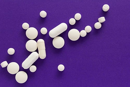 A varitey of white pills on a purple surface.
