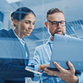 A man and woman look into a laptop the man is holding in his arm 