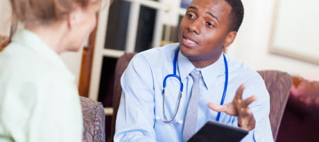 A young doctor holding a computer tablet while talking with a patient.