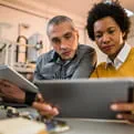 A male and a female health professional look at a tablet the female professional is holding. 