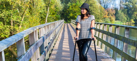 A woman standing with elbow crutches on a bridge as she looks into the distance