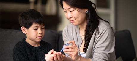 A mother is helping a five year old boy check his blood sugar levels with a fingerstick