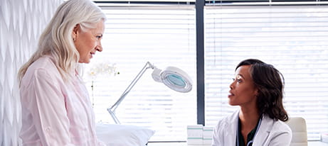A female  physician sitting down talks with a female patient sitting on an exam table